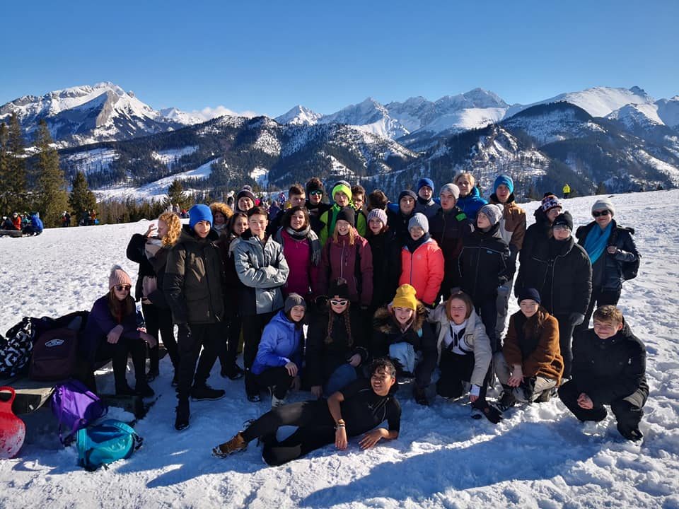 Grupa młodych w zimowych kurtkach na śniegu, w tle ośnieżone Tatry